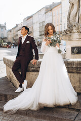 An international wedding couple, a European bride and an Asian groom walk around the city together.