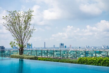Outdoor rooftop swimming pool with green tree garden and city view in sunny day. Building and...