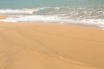 Blue sea waves with foam on yellow sand beach.