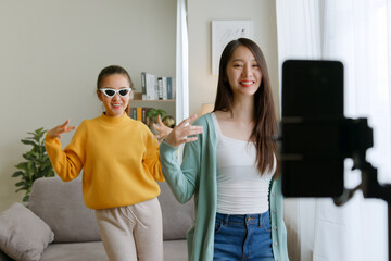 Asian young woman with her friend created her dancing video by smartphone camera together. To share...