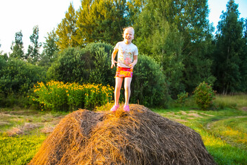 Naklejka na ściany i meble A happy little girl having a good time in the countryside. Child on a haystack. 