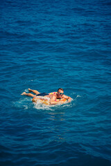 A young man floats on an inflatable air ring circle in the sea with blue water. Festive holiday on a happy sunny day.