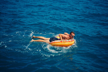 A young man floats on an inflatable air ring circle in the sea with blue water. Festive holiday on a happy sunny day.