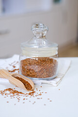 Flax seeds in a glass jar with wooden spoon on a linen napkin in the kitchen. Ingredient for flaxseed porridge and jelly. Minimalistic simple natural light template. Superfood. Organic eco healthcare.