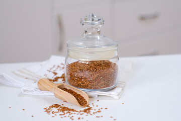 Flax seeds in a glass jar with wooden spoon on a linen napkin in the kitchen. Ingredient for flaxseed porridge and jelly. Minimalistic simple natural light template. Superfood. Organic eco healthcare.