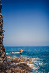 A young man stands on the rocks overlooking the open Mediterranean Sea. A guy on a warm summer sunny day looks at the sea breeze