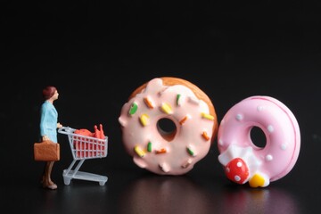 miniature figurine of a woman with shopping cart and giant donuts on a black background