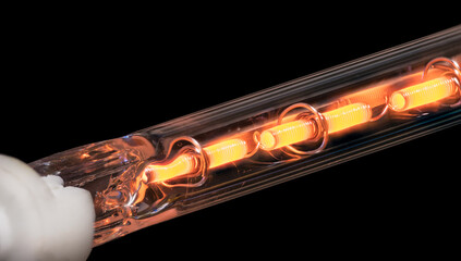 Glowing coiled resistance wire inside heating element on a black background. Closeup of orange hot...