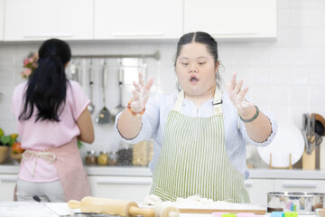 down syndrome teenage girl clapping hands and sprinkling white flour for making a bread in a kitchen