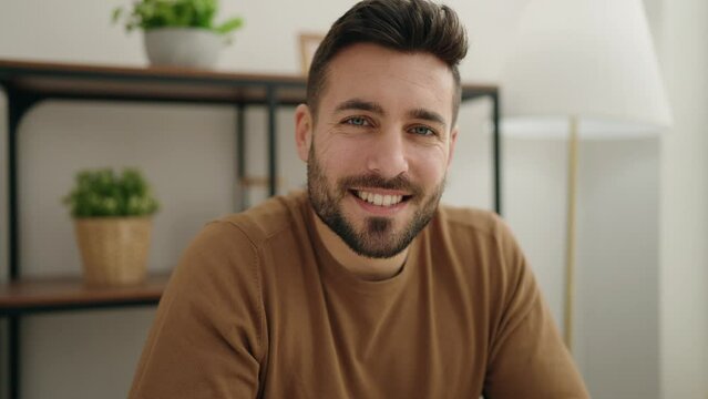 Young hispanic man smiling confident sitting on table at home