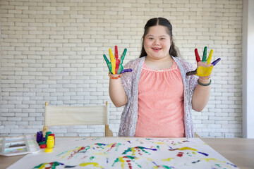 down syndrome teenage girl showing painted hands, drawing a picture on paper
