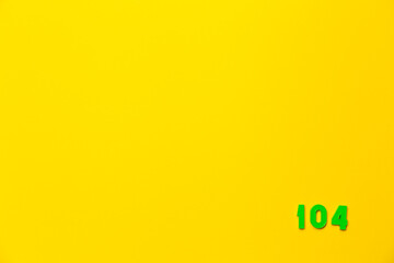 Numeral 104 on a yellow background. Copy space. A green plastic toy number one hundred four is right corner located. Math symbol. Page. Digit. Calendar day. Counting game. Birthday postcard