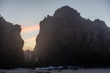 Setting sun behind the rocks at Pfeiffer Beach with orange clouds in the sky.