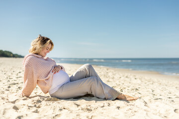 Fototapeta na wymiar Pregnant woman in sweater sitting on seashore and relaxing