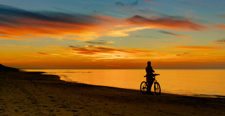 Fototapeta na wymiar Silhouette of cyclist on beach against backdrop of sunset at sea shore