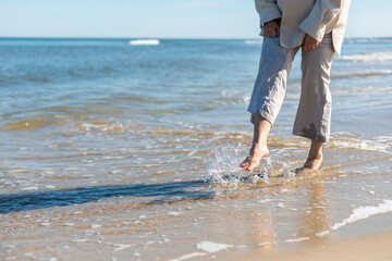 Woman in linen trousers walking barefoot on sandy beach