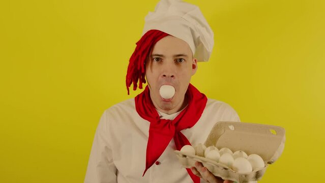 A man with red dreadlocks stands with a chicken egg in his mouth. A confident young chef in a white shirt and red tie holds chicken eggs