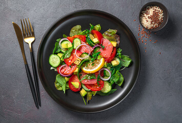 Fresh vegetable salad with salmon, fresh herbs and seeds on a dark background.