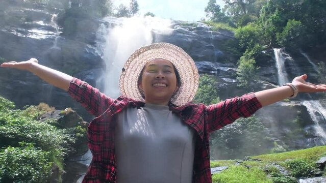 Happy hipster woman in straw hat and red plaid shirt enjoying nature at The Wachirathan waterfall in Doi Inthanon National Park in Chiang Mai northern thailand. Thailand travel Concept