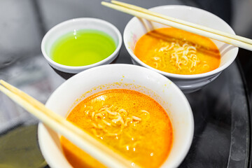 Macro closeup texture of two spicy red ramen noodle soup white bowls with chopsticks Japanese asian meal and green tea cup