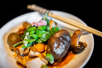 Traditional Japanese food dish macro closeup with mushrooms, tofu and green onions of plate chopsticks in house ryokan restaurant hotel with black background of lacquered table