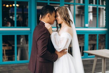 Wedding day. Beautiful European bride and her Asian groom posing against the backdrop of cafes and large windows.