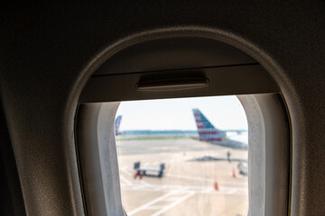 Aerial high angle above view from airplane seat pov in American flight with glass open window in airport runway with other planes