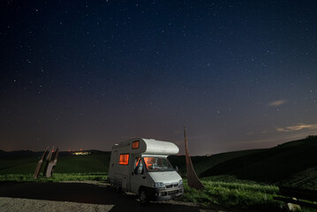 Night sky in the cultivated hill range and cereal crop fields of Tuscany, Italy. Stars over camper...
