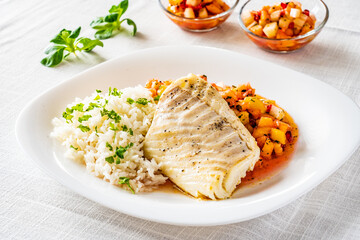 Fish dish - fried cod fillet with boiled white rice and fresh fruit salsa on white table
