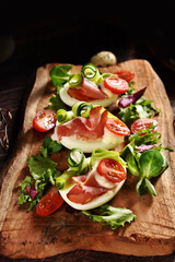 Egg halves with prosciutto ham and vegetables on rustic wooden board