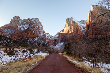 Selective focus early morning winter view of dirt road surrounded by bare trees and red mountains with dusting of snow in Zion National Park, Utah, USA