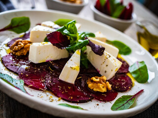 Beetroot carpaccio with goat cheese, greens and walnuts on wooden background

