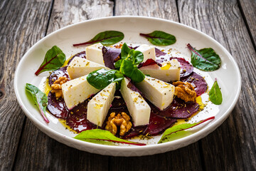 Beetroot carpaccio with goat cheese, greens and walnuts on wooden background
