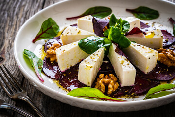 Beetroot carpaccio with goat cheese, greens and walnuts on wooden background
