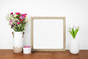 Mock up square wood frame with vases of cut flowers and succulent plant. Wooden shelf against a...