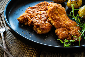 Breaded fried pork chop with potatoes and rosemary  on wooden table
