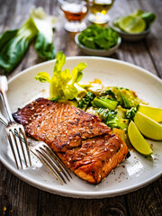Fried teriyaki salmon steak with pak choi and lime on wooden table

