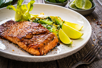 Fried teriyaki salmon steak with pak choi and lime on wooden table
