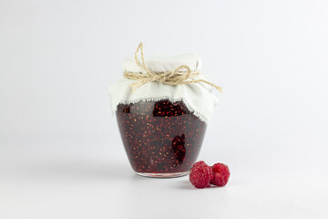 Raspberry jam in glass jar and fresh raspberries on white background.