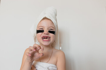 Portrait of a little girl after spa procedures with a towel on her head and with patches on her eyes ryaa like a tiger into the camera