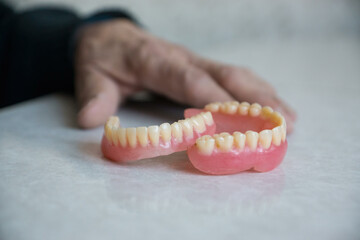 Close-up of dentures on the table next to the hand of an elderly man.Tooth prosthetics concept. Selective focus, shallow depth of field