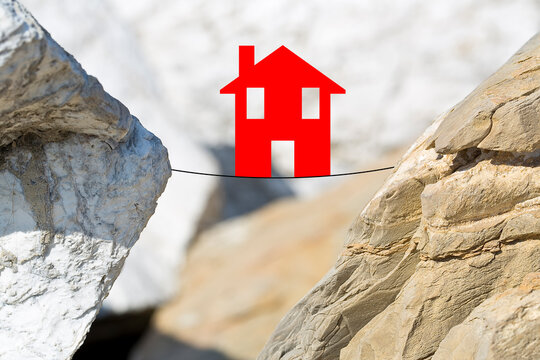 Dangers and pitfalls of a house - real estate market crisis - concept with a little house above a cable balanced on a ravine