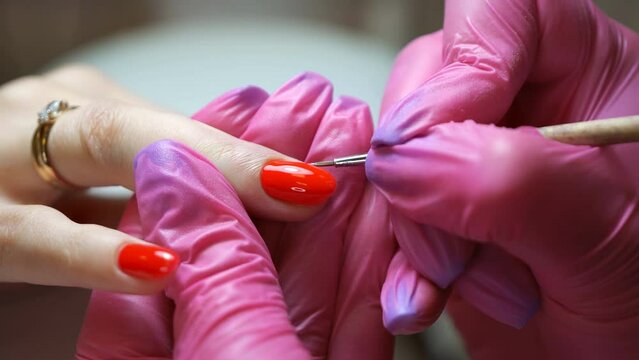Close up of manicure master in rubber gloves applying red nails in the beauty salon.