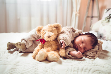 Infant multiethnic baby boy sleeping on a bed. Looking cozy with teddy bear