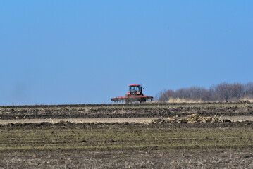 Obraz premium Tractor plowing the soil in spring closing the moisture, preparing the land for sowing. Agriculture concept photo