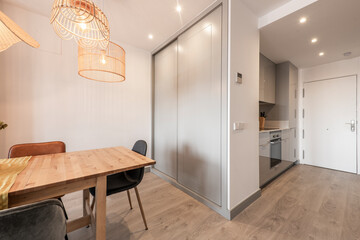 Living room with wooden dining table, wicker lamps, built-in wardrobe with sliding gray wooden...