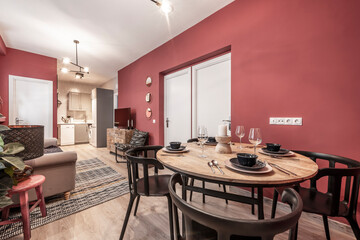 Apartment with living room and open kitchen with round wooden dining table, food service set and red walls