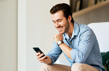 Looks like theres a lot buzzing online. Shot of a handsome young man texting on a cellphone at home.