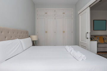 Bedroom with double bed, fabric upholstered headboard and built-in wardrobe with trunk and white wooden doors