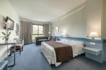 bedroom with large bed, brown blanket, blue wooden decoration, tv on the wall and blue carpet